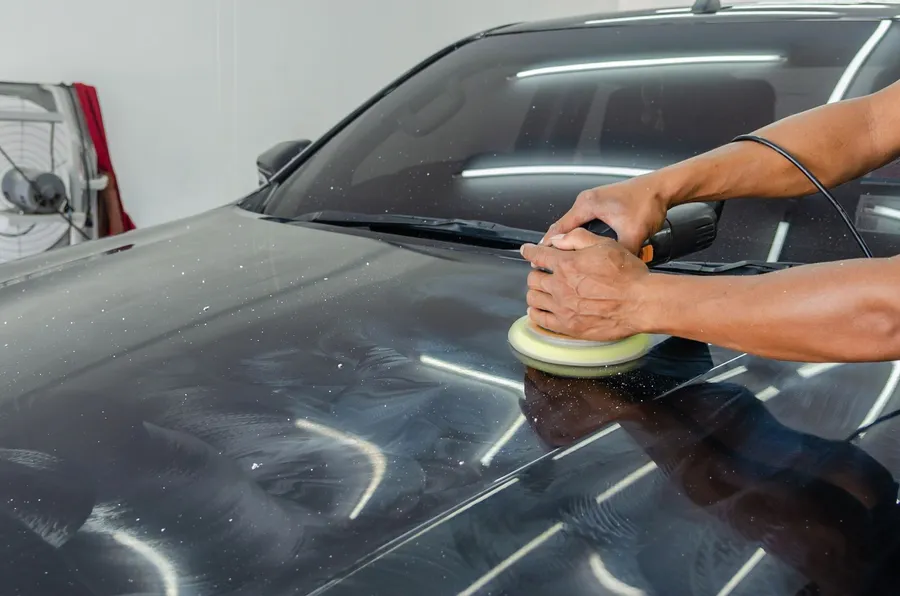 Hands guiding a polisher across a dark car hood