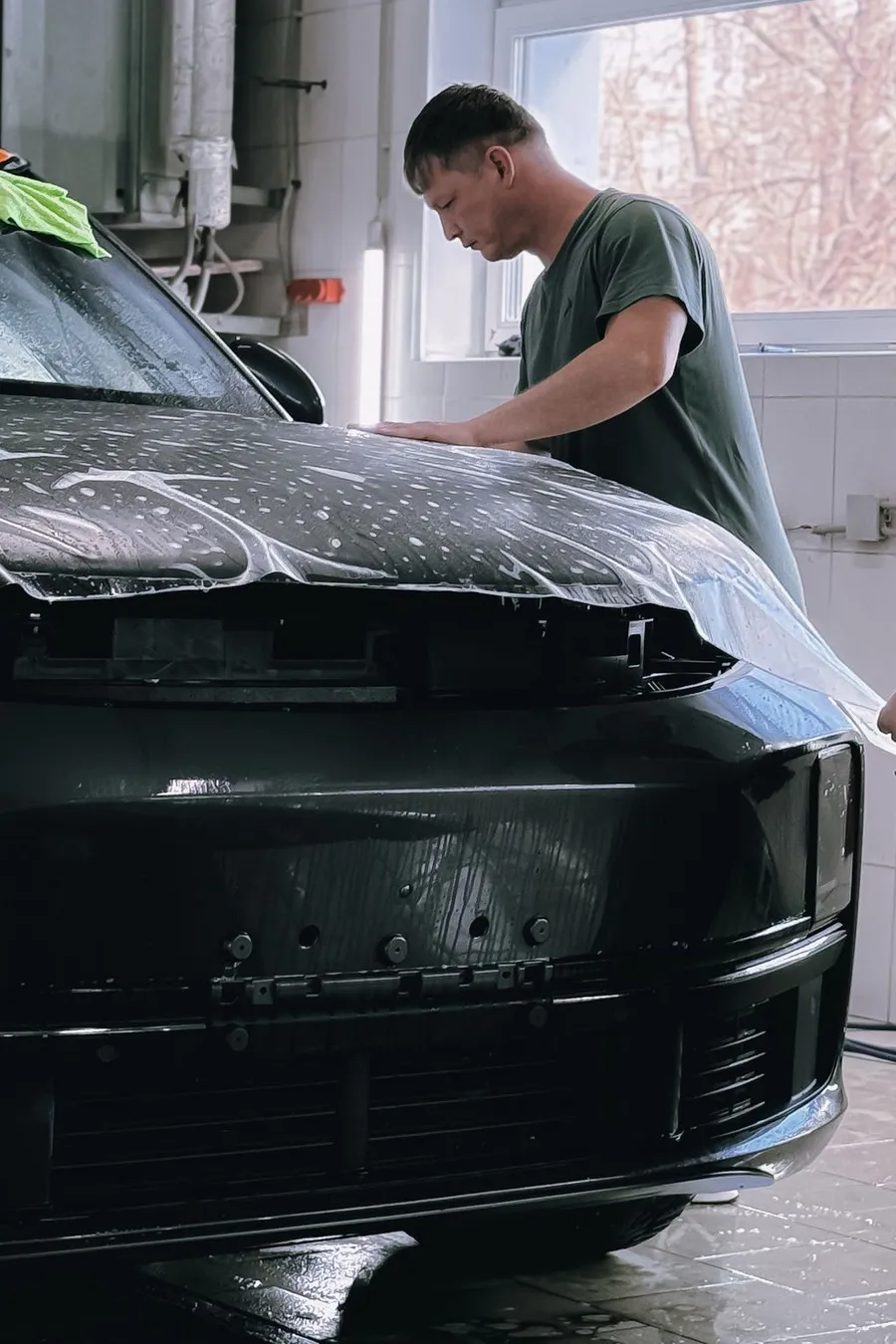 Installer smoothing clear paint protection film onto the hood of a black car
